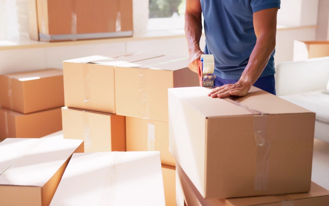 Man packing up house and adding packaging tape to a box with other moving boxes around him